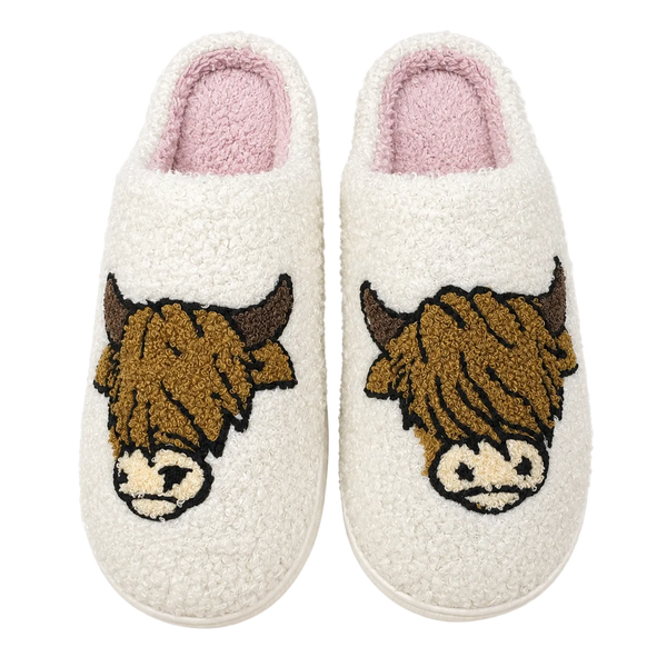 Pair of white slippers with highland cow designs on a white background